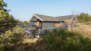 A wooden cabin with a deck, a grill, and a stack of firewood. - Lovely home in Ringkøbing with sauna (Ringkøbing)