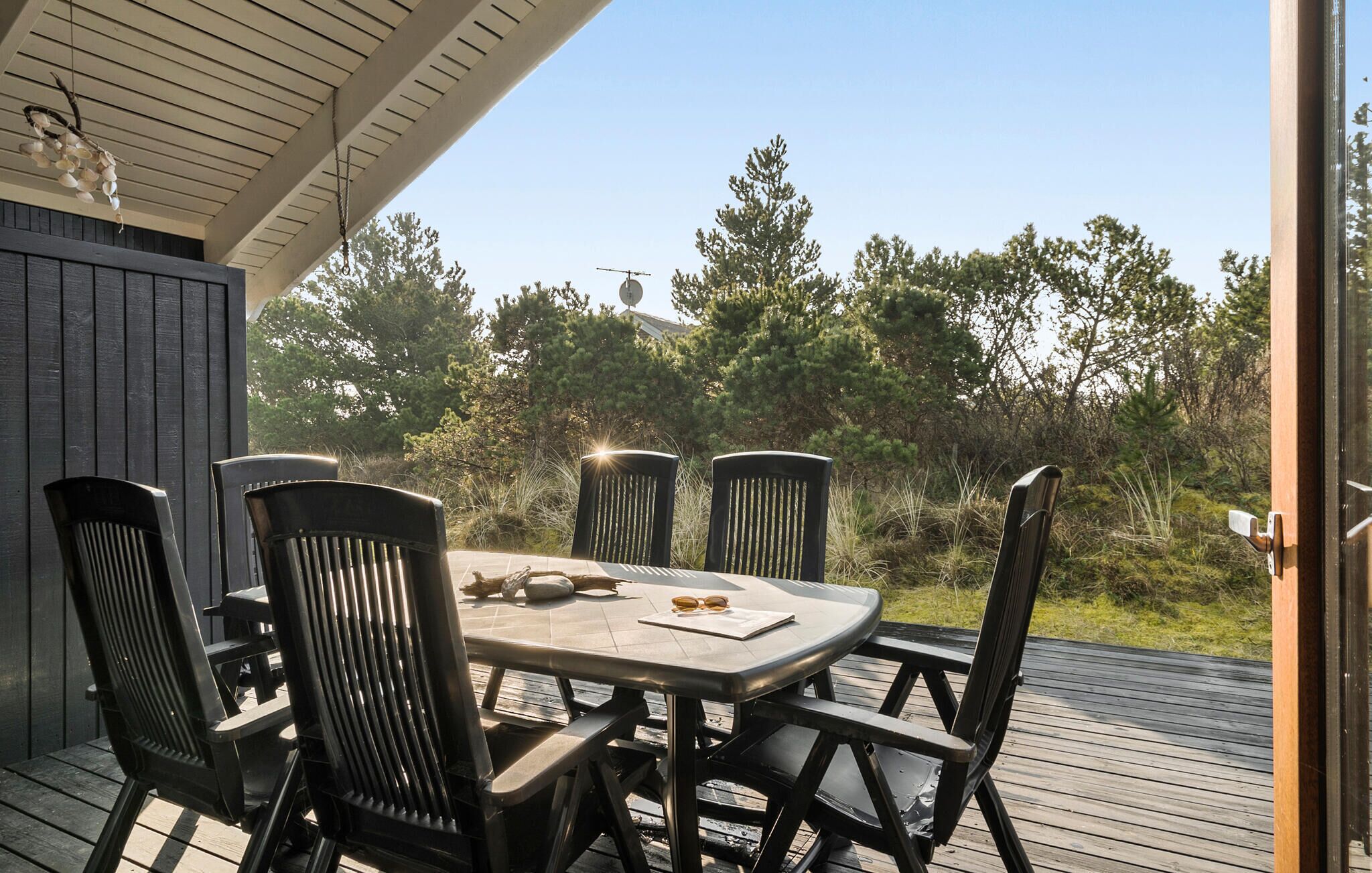 Patio esterno con tavolo e quattro sedie, circondato da un pavimento in legno e vegetazione.