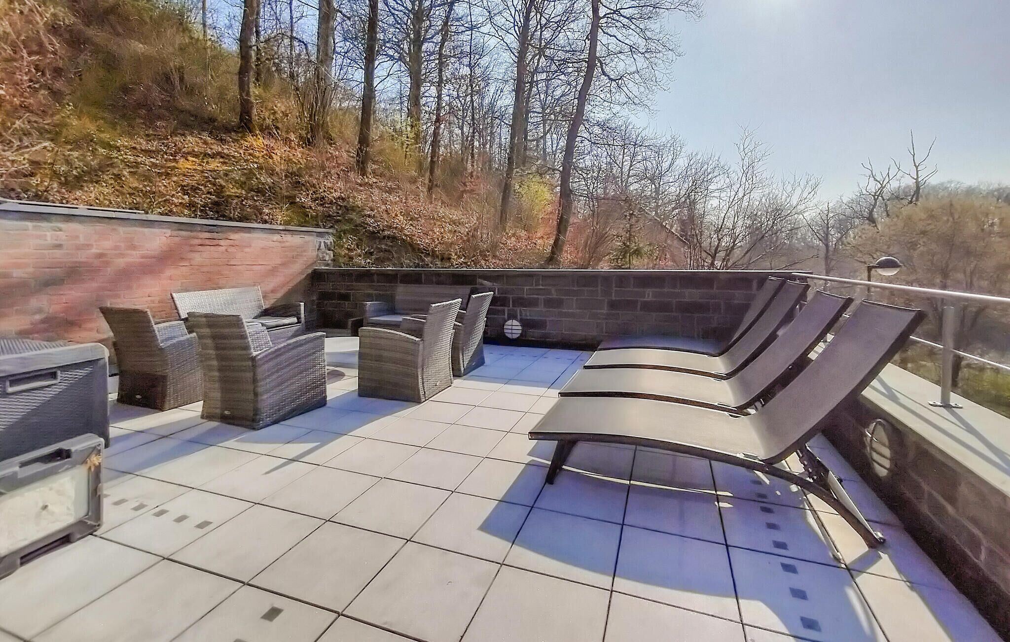 Un patio al aire libre con pared de ladrillo, suelo de baldosas y mobiliario exterior, incluyendo sillas y una mesa.