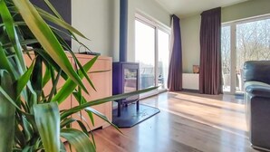 A living room with a flat-screen TV, a wooden cabinet, a large potted plant, and a view of the outdoors through a sliding glass door. - Stunning home in Durbuy with sauna (Durbuy)