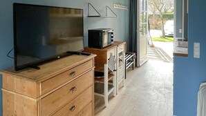 Una habitació amb televisió sobre un moble de fusta, una taula petita amb microones i una porta que dona a l'exterior.