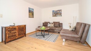 A living room with a wooden cabinet, a brown sofa, a coffee table, and two wall-mounted paintings. - Ferienwohnung in Sankt Koloman (Sankt Koloman)