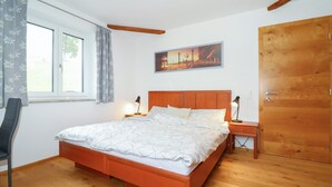 A bedroom with a wooden bed, a nightstand with a lamp, a window with curtains, and a door. - Ferienwohnung in Sankt Koloman (Sankt Koloman)