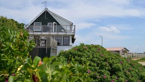 Una casa de dos pisos con balcón, rodeada de vegetación y un cielo despejado.
