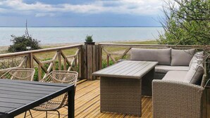 Una terraza de madera con una mesa, sillas, un sofá y vista al mar.