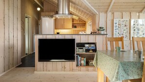 A cozy cabin interior with a wooden interior, a built-in TV, a dining area with a table, and a kitchen with wooden cabinets and a stove.