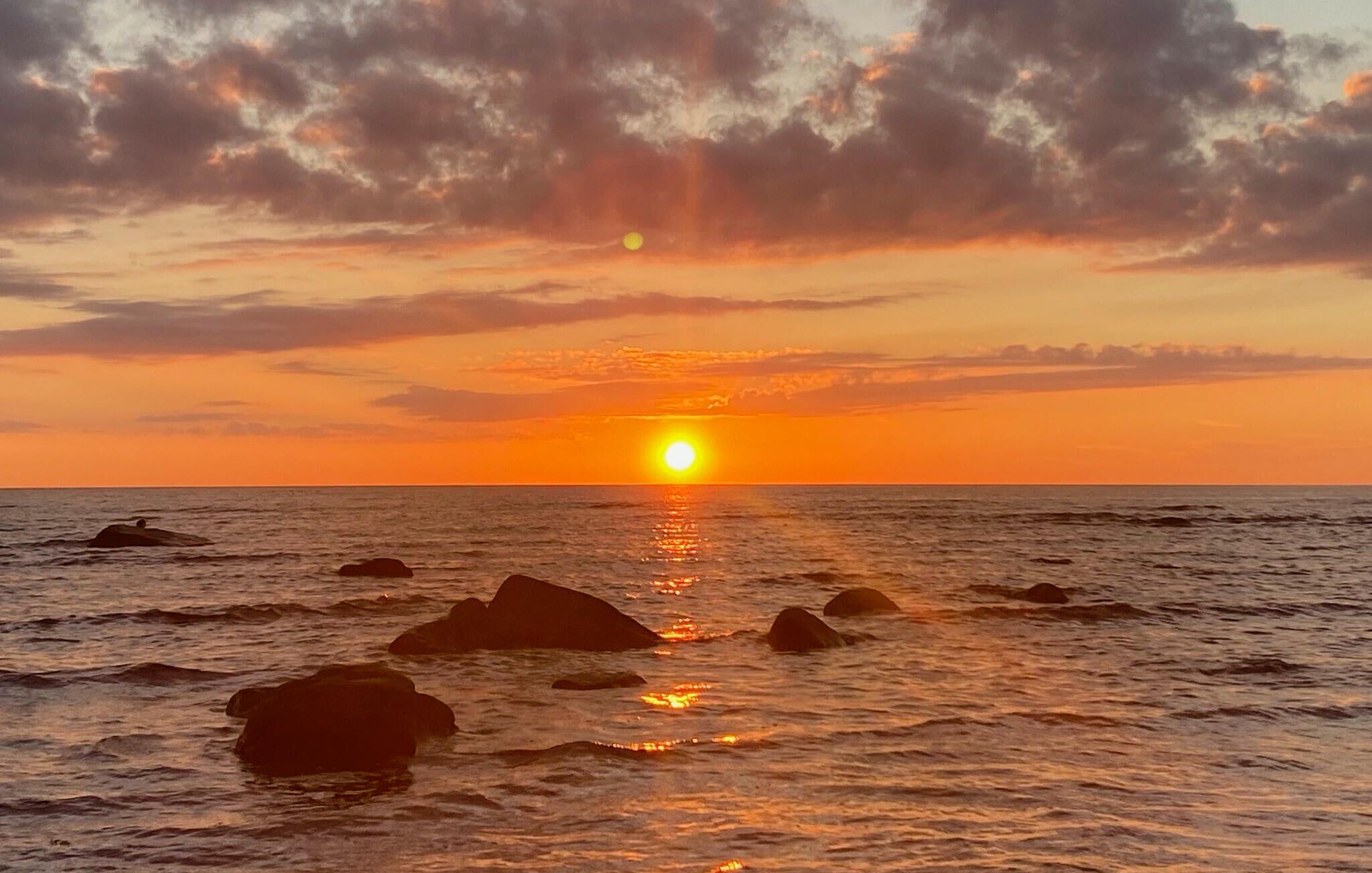 A sunset over the ocean with rocks in the water.