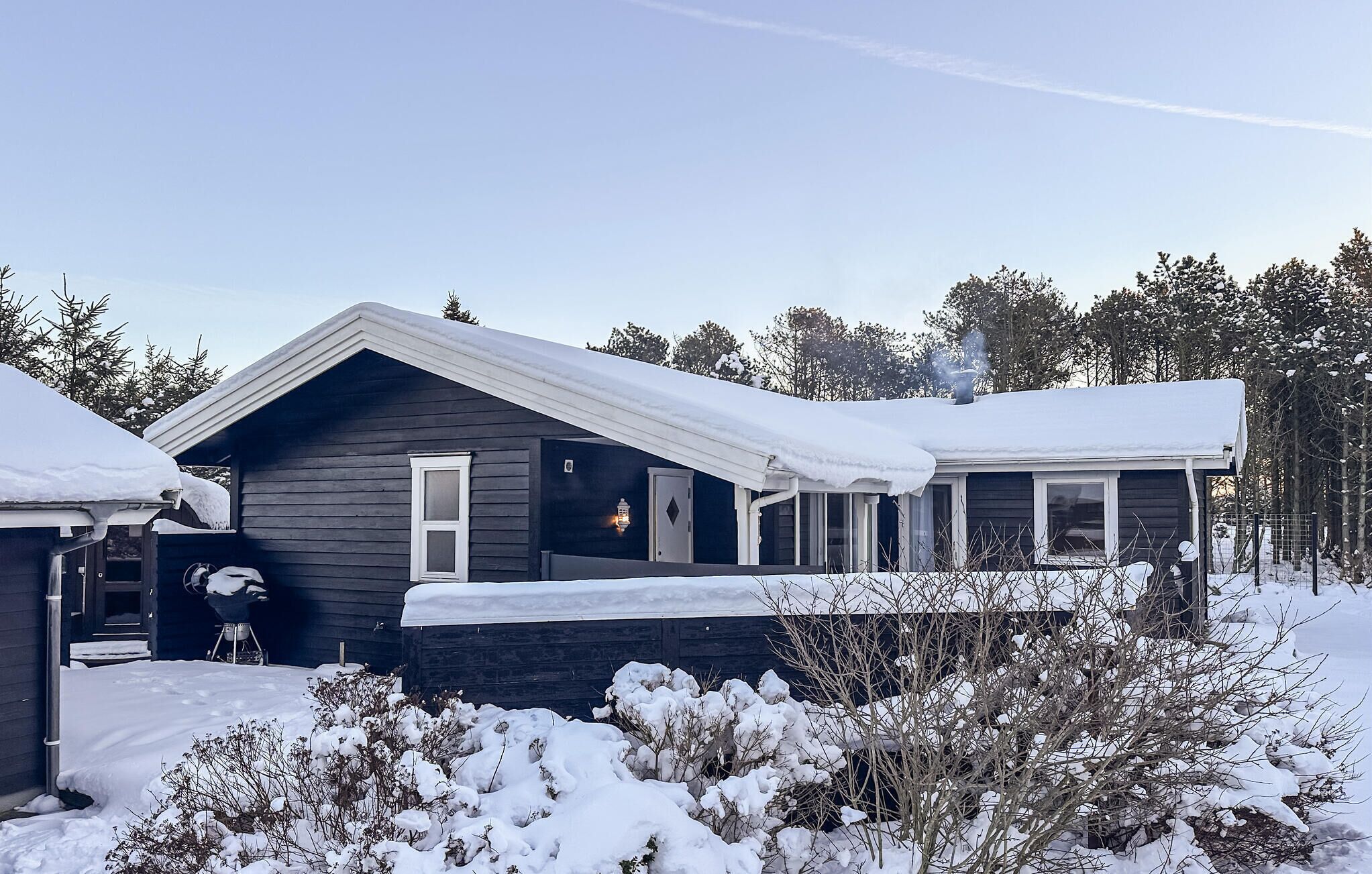 A two-story house with a dark exterior, covered in snow.