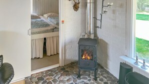 A cozy room with a stone floor, a bed with white bedding, a wood-burning stove, and a window with a view of greenery. - 4 bedroom amazing home in Hurup Thy (Hurup Thy)