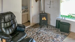 A cozy room with a stone floor, a black leather chair, a wood-burning stove, and a window with a view of greenery. - 4 bedroom amazing home in Hurup Thy (Hurup Thy)