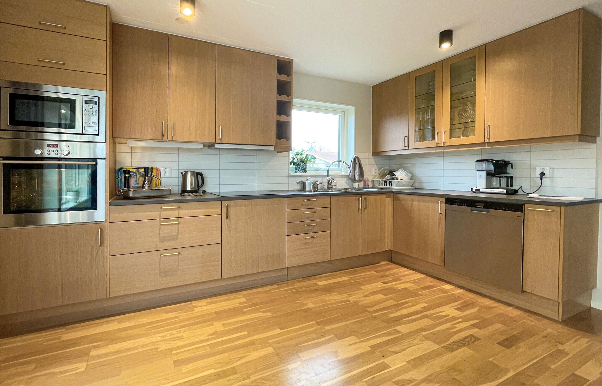 A modern kitchen with wooden cabinets, stainless steel appliances, and a wooden floor.