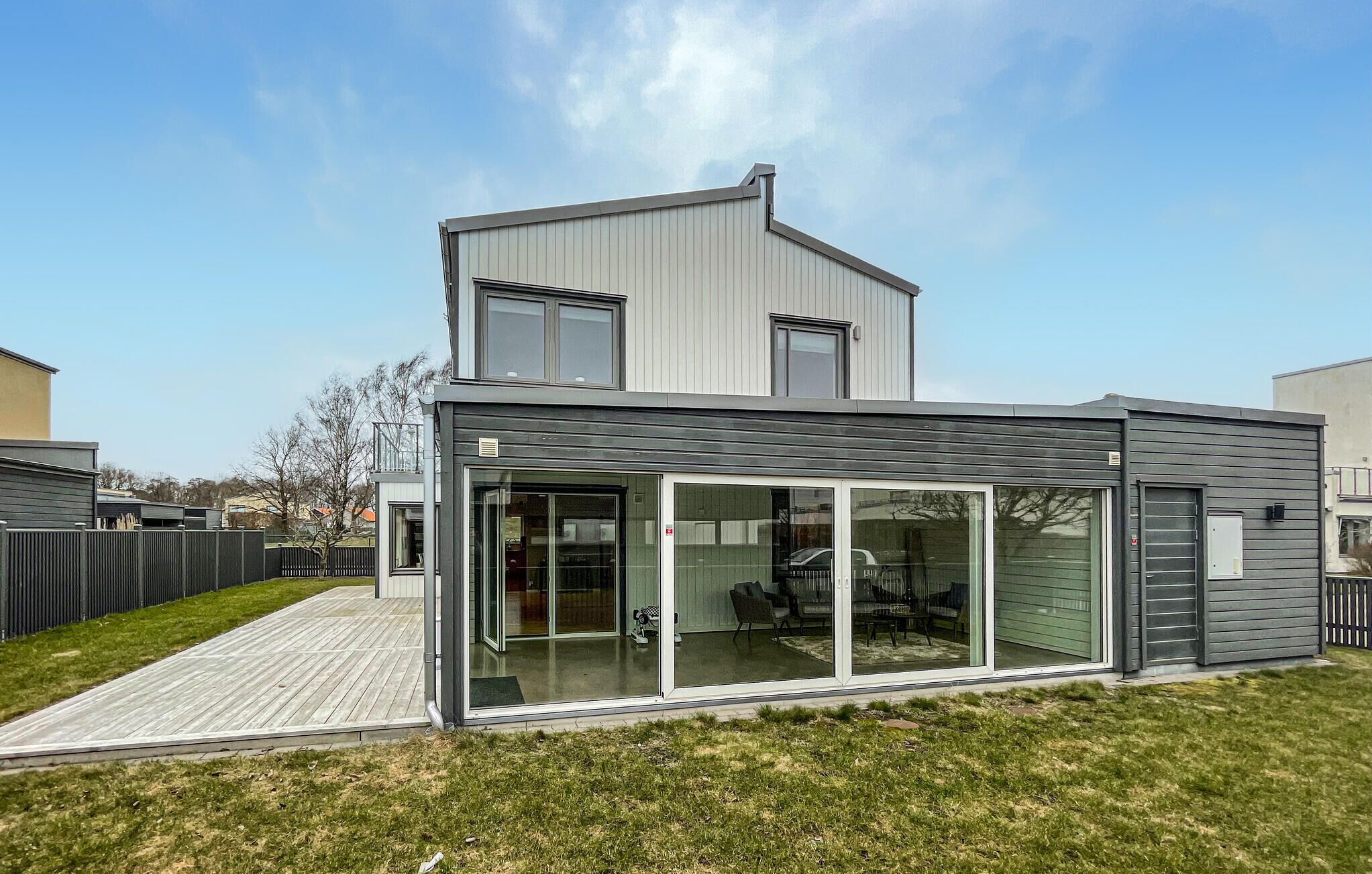 Ett modernt hus i två våningar med en stor entré bestående av en glasdörr och en täckt uteplats.