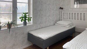 A small, single-bed room with a grey mattress, white bedding, a white headboard, a window with blinds, and a potted plant on the windowsill. - 1 bedroom stunning home in Mullsjö (Mullsjö)