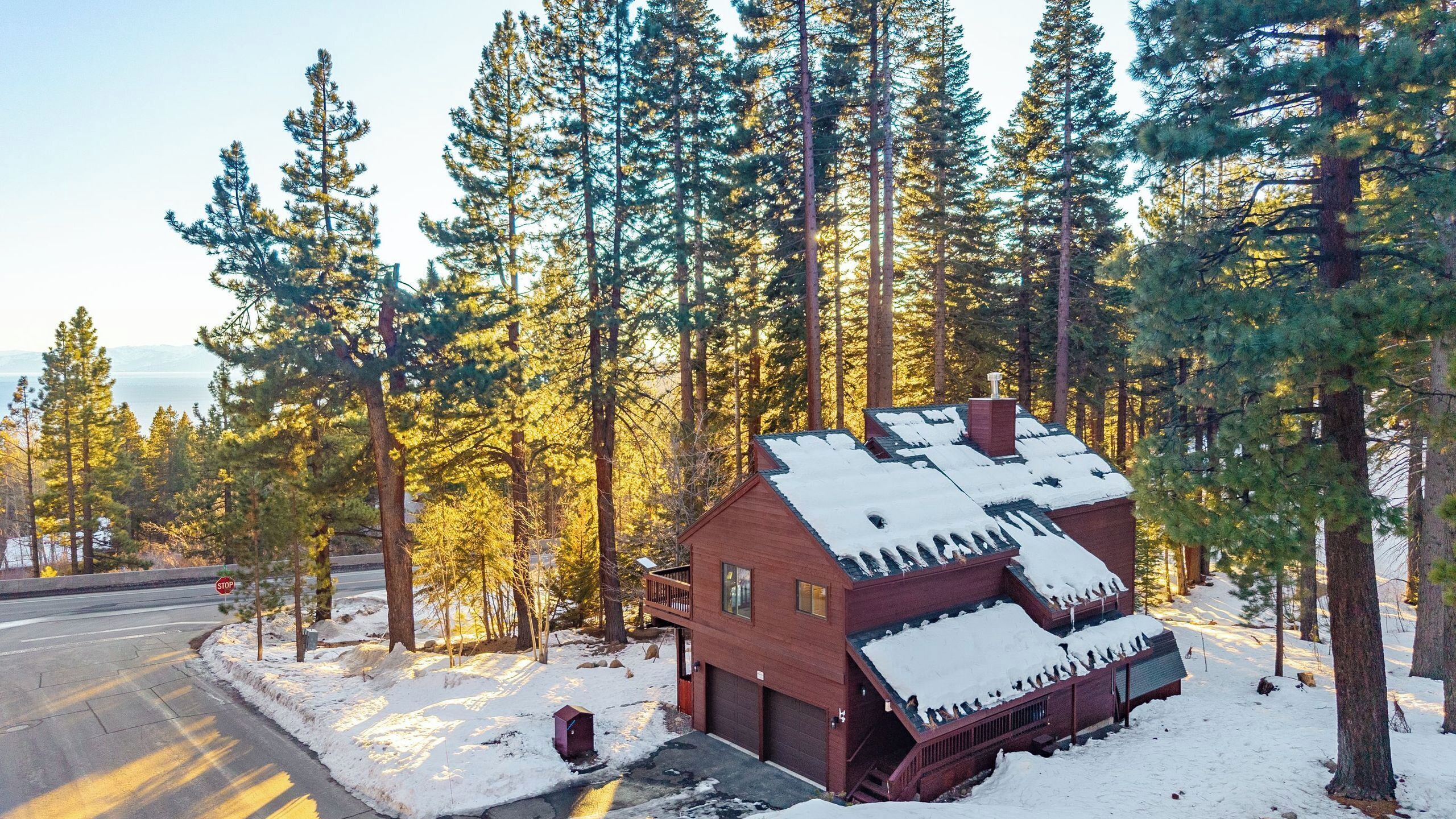 A cabin with a snow-covered roof, surrounded by tall pine trees.
