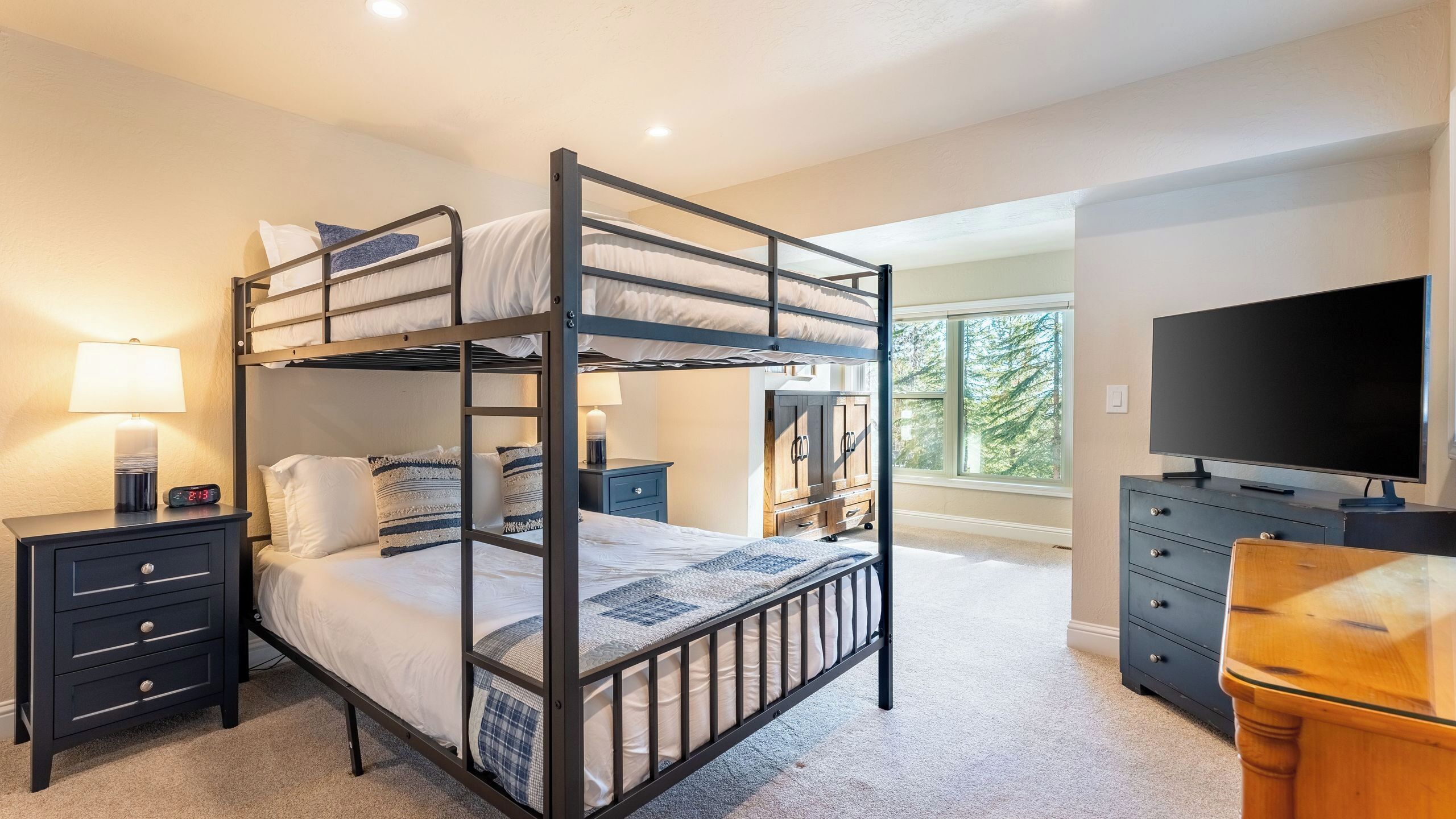 A bunk bed room with a TV, dresser, and window with a view.