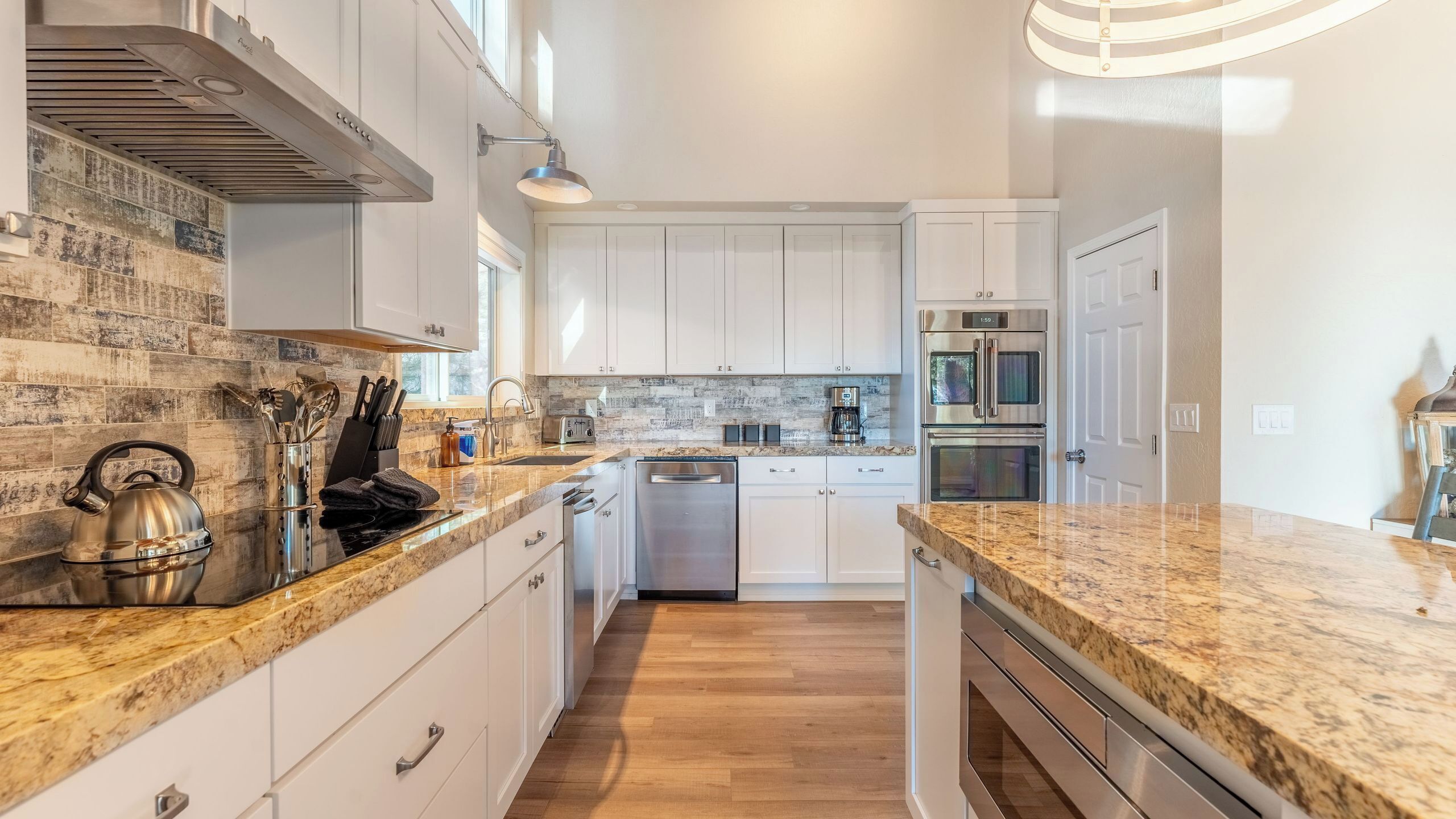 A modern kitchen with white cabinets, granite countertops, stainless steel appliances, and a visible clock.