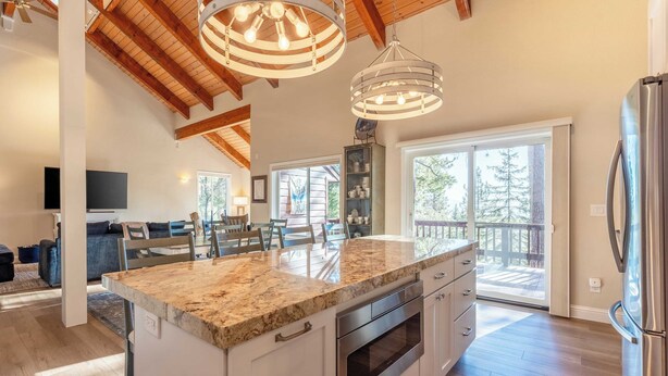 A spacious kitchen with a large island, built-in oven, and stainless steel refrigerator. There is a dining area with a table and chairs, and a balcony with a view of trees. - Views + Mins to Skiing, Lake, & Incline Village Incline Serenity by Avantstay (Incline Village)