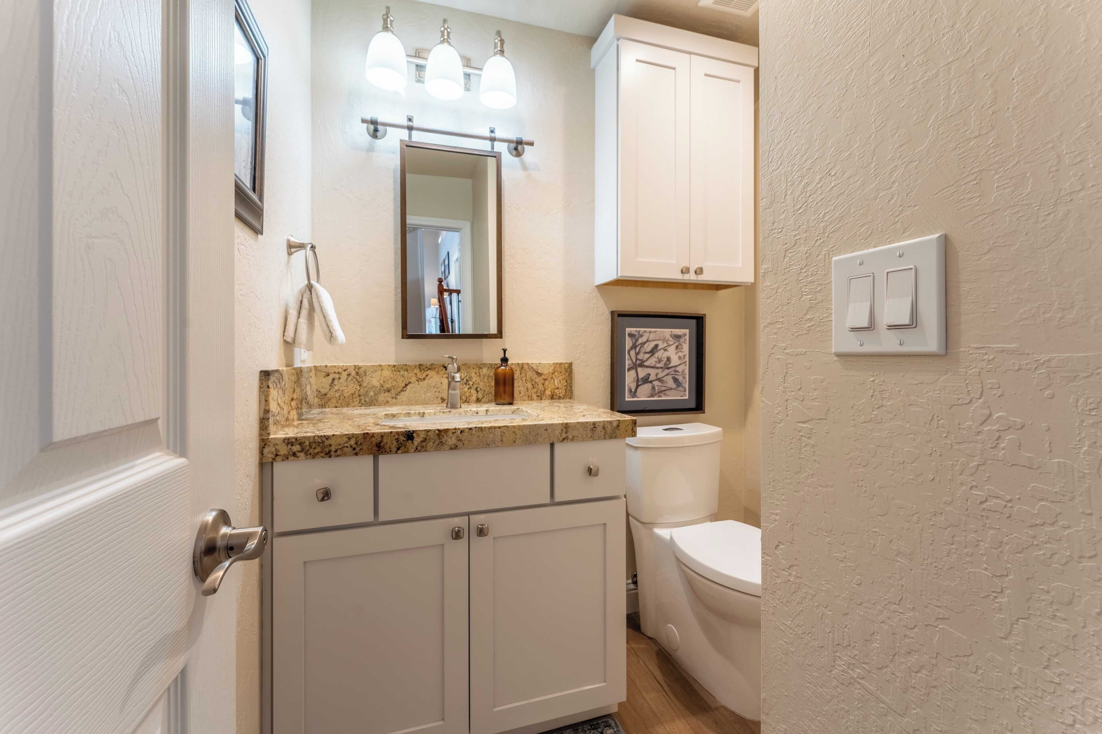 Une salle de bain avec un comptoir en marbre, un lavabo, un miroir, des toilettes et un meuble de rangement.