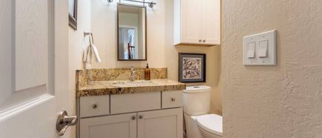 A bathroom with a marble countertop, a sink, a mirror, a toilet, and a cabinet.
