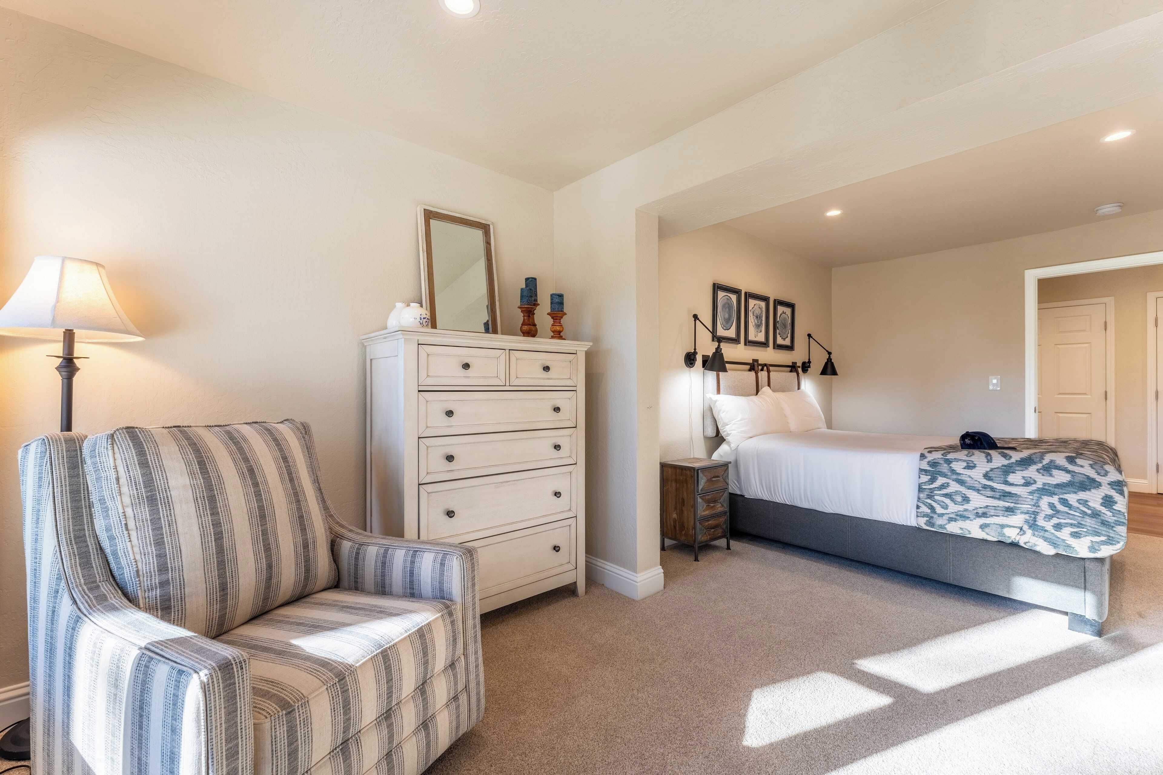 Un dormitorio con cama, cómoda, silla y lámpara.