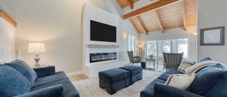 Una sala de estar moderna con sofás azul oscuro, un televisor de pantalla plana, una chimenea y un techo de madera.