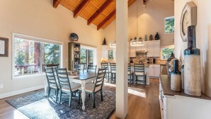 A spacious kitchen with wooden beams, a dining area with a large table and chairs, and a view of the outdoors through large windows. - Views + Mins to Skiing, Lake, & Incline Village Incline Serenity by Avantstay (Incline Village)