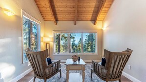 A cozy room with a wooden ceiling, large windows with a forest view, two wooden chairs, a small table, and a lamp. - Views + Mins to Skiing, Lake, & Incline Village Incline Serenity by Avantstay (Incline Village)
