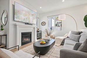 A modern living room with a fireplace, a flat-screen TV, a round coffee table with decorative items, a sofa, and a floor lamp. - Stylish Multi-Level Condo with Fireplace & Spacious Living (Santa Barbara)