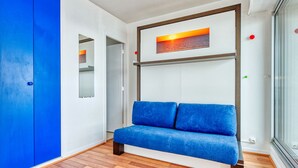A modern room with a blue sofa, wooden flooring, a blue wardrobe, and a framed picture on the wall.