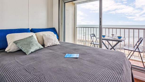 A hotel room with a large bed, a balcony with a table and chairs, and a view of the sea.