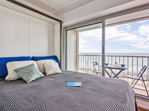 Habitación de hotel con una cama grande, un balcón con mesa y sillas, y vista al mar.