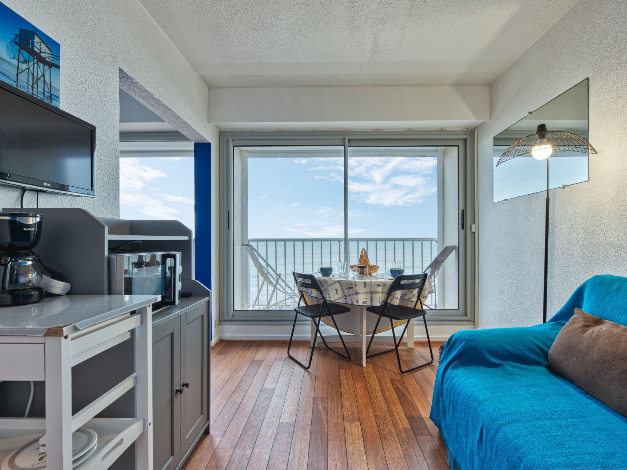 Un balcon avec une table à manger, des chaises et un canapé. On y trouve également une machine à café et un téléviseur posés sur un meuble.