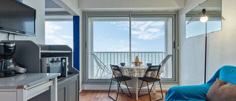 Un balcon avec une table à manger, des chaises et un canapé. On y trouve également une machine à café et un téléviseur posés sur un meuble.