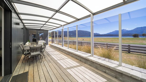 A covered outdoor area with a table and chairs, a view of mountains and a field.
