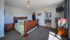 A bedroom with a wooden bed, a nightstand, a dresser, a mirror, and a TV on the wall.