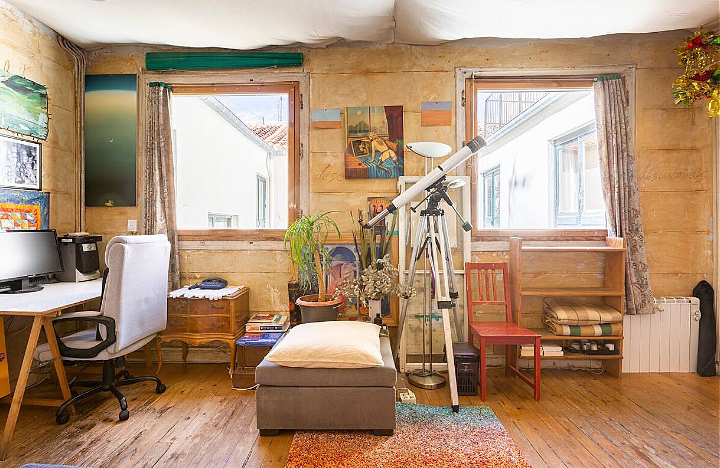 Une pièce confortable avec un bureau en bois, un ordinateur, une chaise, un petit canapé, un télescope et une fenêtre avec des rideaux.