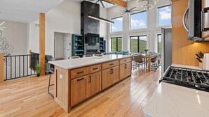 A spacious kitchen with wooden cabinets, a large island, and a modern stove. - 5 mins to Deadwood|Hot Tub|Game Room (Sturgis)