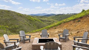 A scenic outdoor seating area with Adirondack chairs and a stone fire pit, overlooking a hilly landscape with distant mountains. - 5 mins to Deadwood|Hot Tub|Game Room (Sturgis)