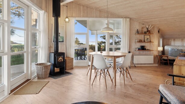 A cozy room with a large window, a fireplace, a dining table with chairs, and a wooden ceiling.