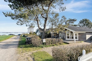 Une propriété située sur la côte, avec un chemin de gravier menant à une maison en bois dotée d’un toit en tuiles, entourée de verdure et offrant une vue sur la mer.