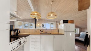 A modern kitchen with white cabinets, a built-in oven, a refrigerator, and two hanging wicker pendant lights.
