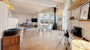 A spacious room with wooden floors, a round dining table, white chairs, a TV, and a large window.