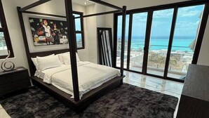 A four-poster bed with a dark, fluffy rug, a ceiling fan, and a large window with a view of the ocean. - White Sky Beach Villas (New Hope)