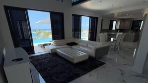 A modern living room with a large sofa, a coffee table, and a view of the ocean. - White Sky Beach Villas (New Hope)