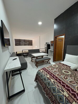 A modern bedroom with a large bed, a desk, a sofa, and a dining area. - Periférico Bodega con Departamento D (Tonalá)