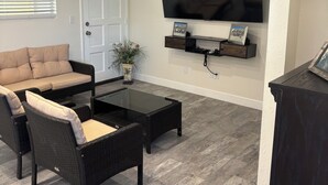 A living room with a black sofa, a glass coffee table, and a flat-screen TV mounted on the wall.
