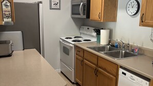 A compact kitchen with wooden cabinets, a stainless steel sink, a microwave, a stove, and a dishwasher.