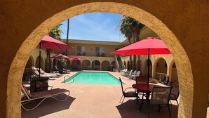 A pool area with red umbrellas, lounge chairs, and a tiled floor.