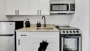 A compact kitchen with white cabinets, a microwave, a stove, and a sink. - La Bella vacations 2 (Fort Lauderdale)