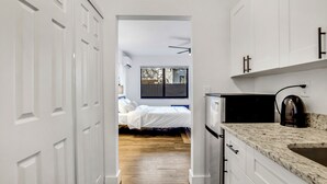 A narrow hallway leading to a bedroom with a bed and a window. A kitchen area with white cabinets and a countertop is visible to the right. - La Bella vacations 2 (Fort Lauderdale)